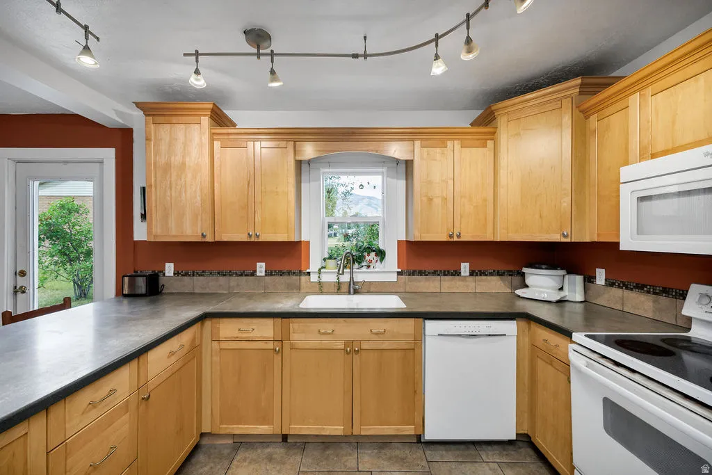 Kitchen featuring wood cabinetry, solid surface countertops, a white built-in dishwasher, white built-in microwave, and track lighting