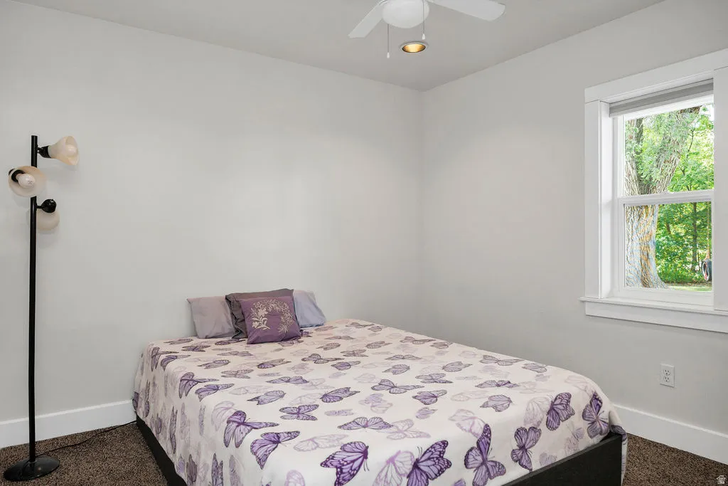 Bright room with neutral wall paint, carpet flooring, a white ceiling fan, and a single window with white trim