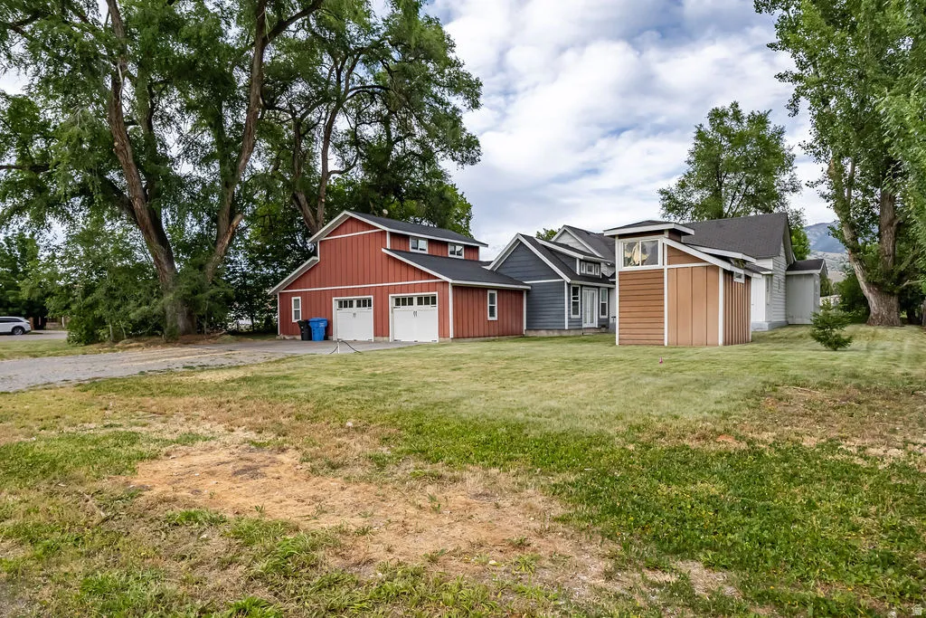 Expansive lot featuring a detached two-car garage with red siding, a separate shed with brown siding, and mature trees providing natural shading