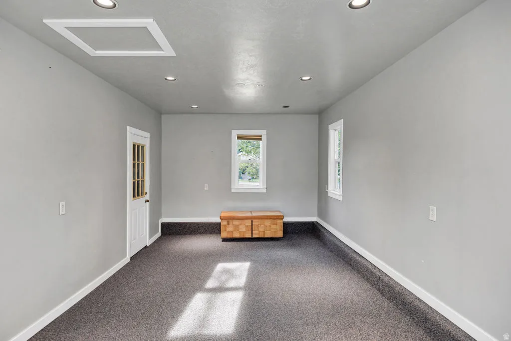 Spacious room on south side of garage featuring gray walls, dark speckled carpet, recessed lighting, and white trim
