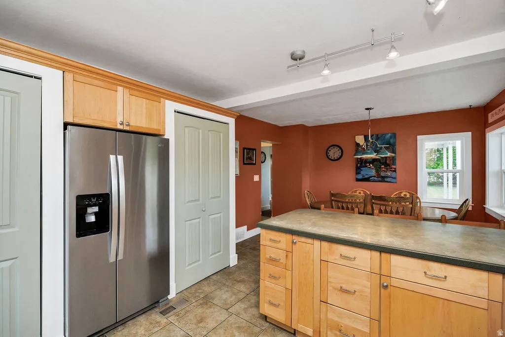 Kitchen featuring a stainless steel side-by-side refrigerator, light wood-finish cabinetry, a central island with a stone-look countertop, track lighting, and tiled flooring