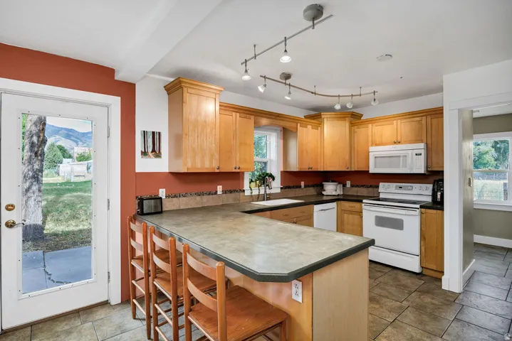 Kitchen featuring wood cabinetry, white appliances, track lighting, and a kitchen island with seating