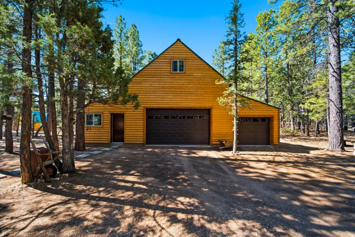 Wood-sided exterior featuring an A-frame roofline, multiple garage doors, and a natural, tree-lined setting