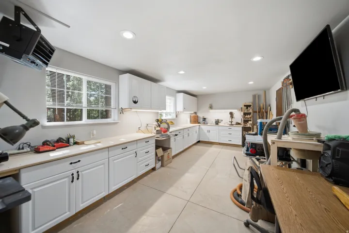 Spacious workshop featuring abundant white cabinetry, light-toned countertops, multiple windows, recessed lighting, and a mounted flat-screen