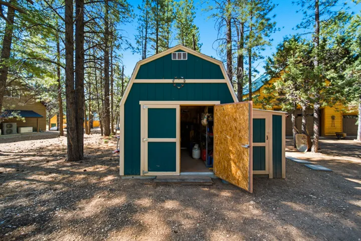 Barn-style storage shed featuring a teal exterior with cream trim, an open main door, and a smaller attached side shed