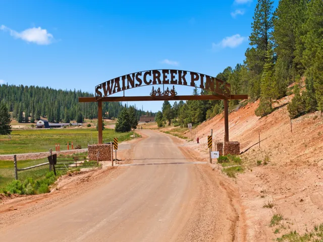 Entryway arch with "SWAINSCREEK PINES" signage, set on a gravel road