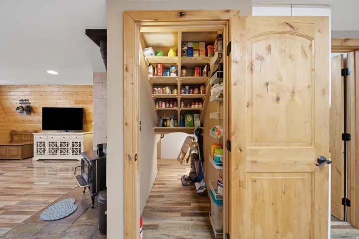 Walk-in pantry with extensive shelving, featuring natural wood doors and framing