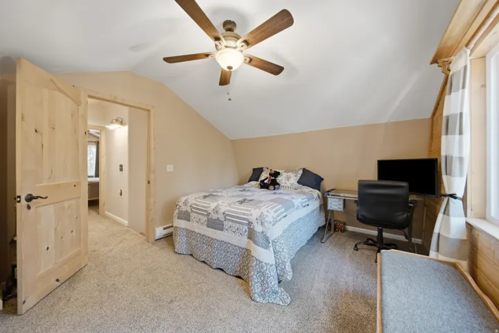 Carpeted room featuring a sloped ceiling, natural wood doors, and a ceiling fan with integrated lighting