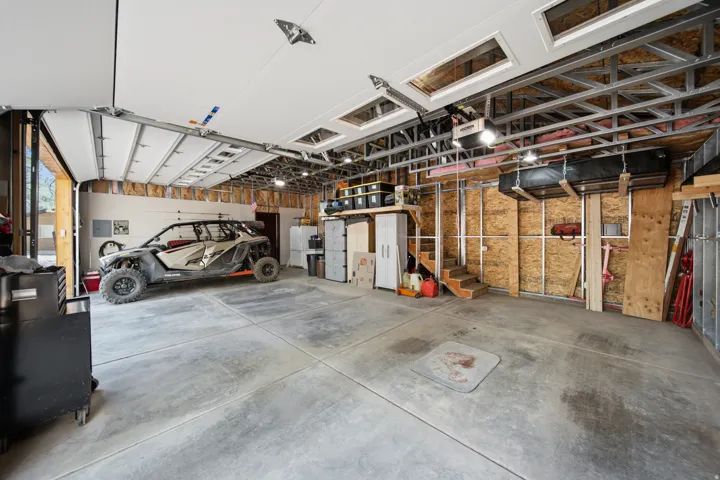 Spacious garage featuring a concrete floor, overhead garage door, exposed metal framing, and a built-in staircase