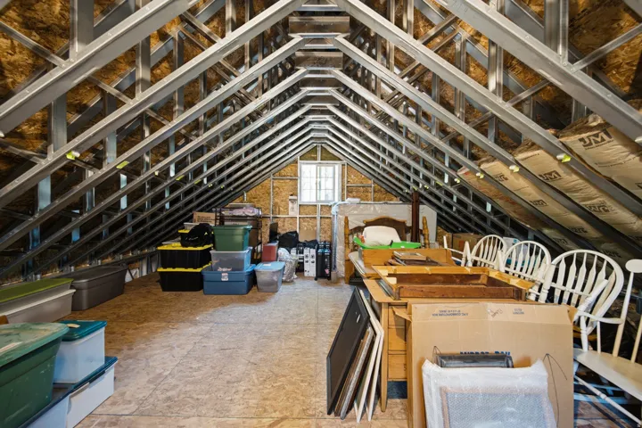 Attic space featuring exposed metal framing, insulation, a window, and wood-finish flooring