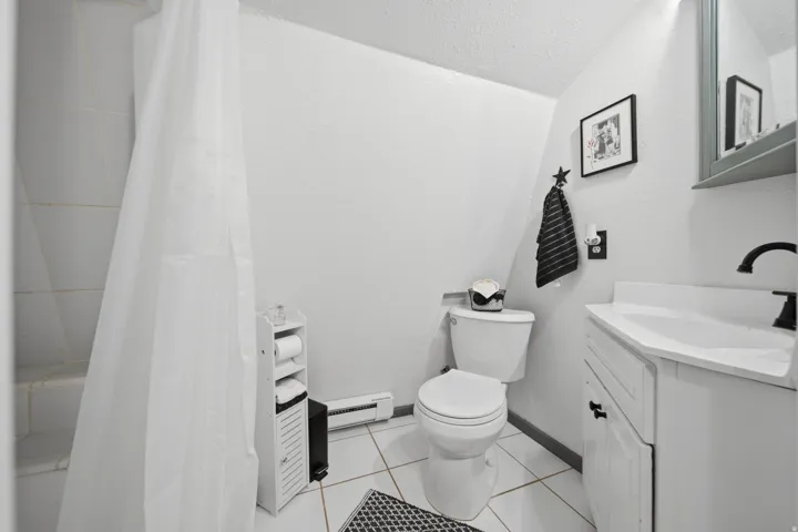 Bathroom featuring white tile flooring, a shower with tiled walls, a white toilet, and a white vanity with a black faucet
