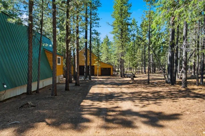 Two-structure property featuring a main A-frame residence with green metal roofing and a second gambrel-roofed building with a garage door