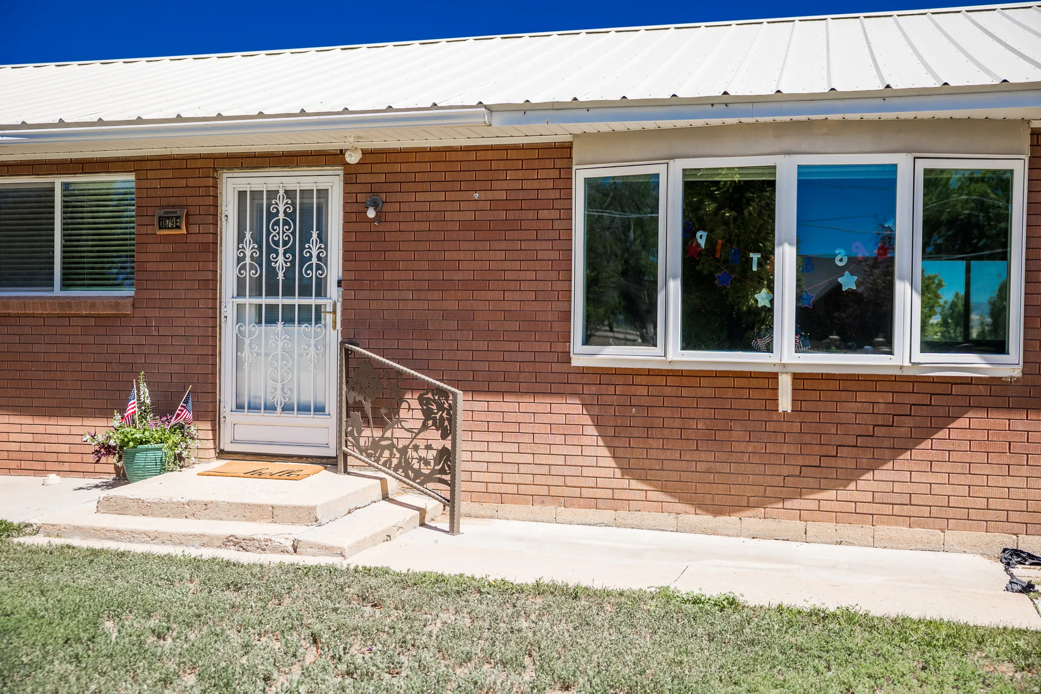 Brick exterior featuring a white metal roof, multiple windows, a security screen door, and a decorative handrail