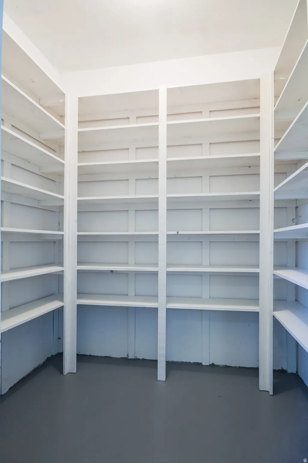 Spacious walk-in pantry with extensive built-in shelving, white painted finishes, and durable gray flooring