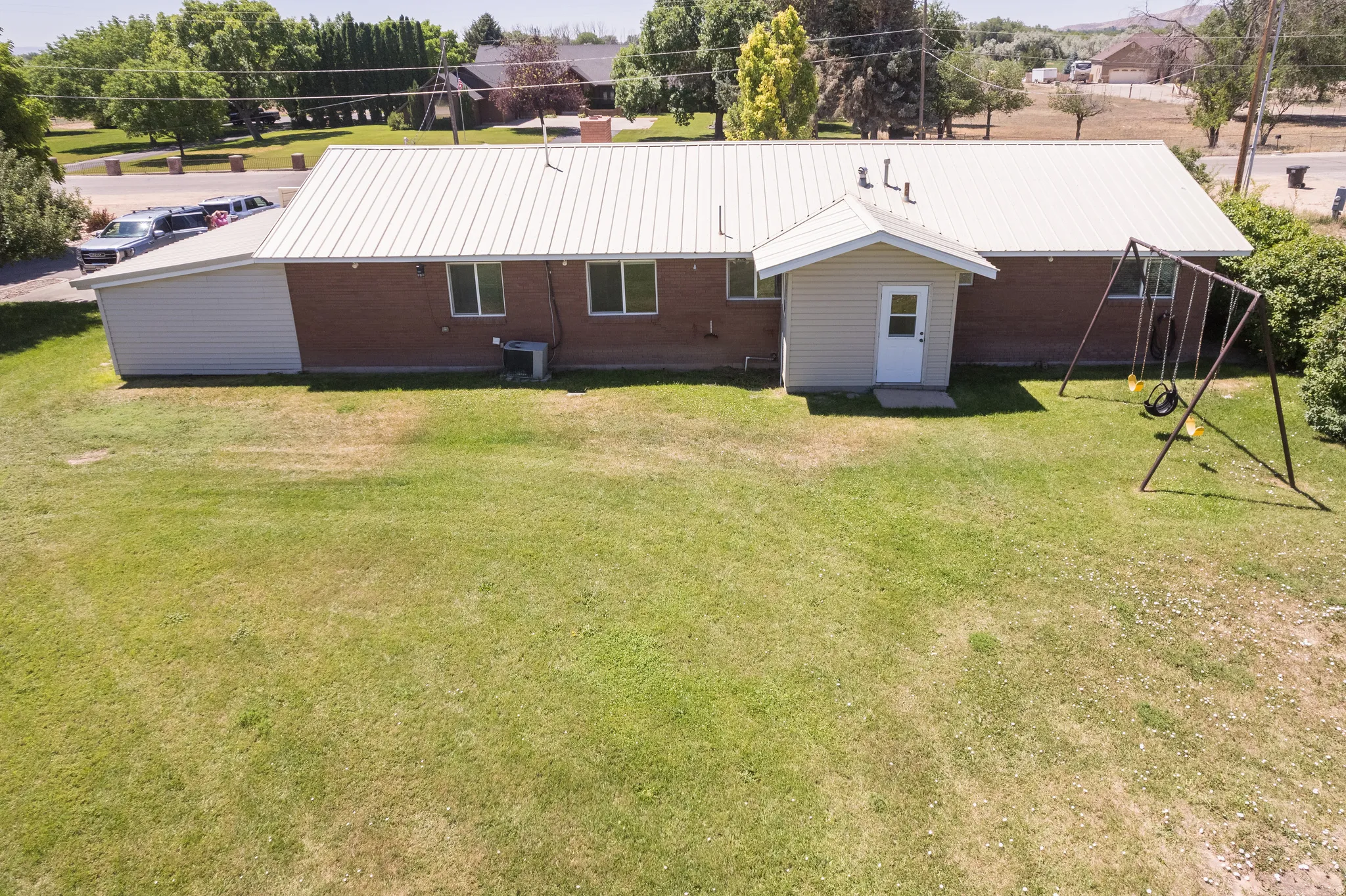 Expansive rear yard featuring a large grass area, a detached auxiliary structure with a white entry door, and a brick exterior with multiple windows