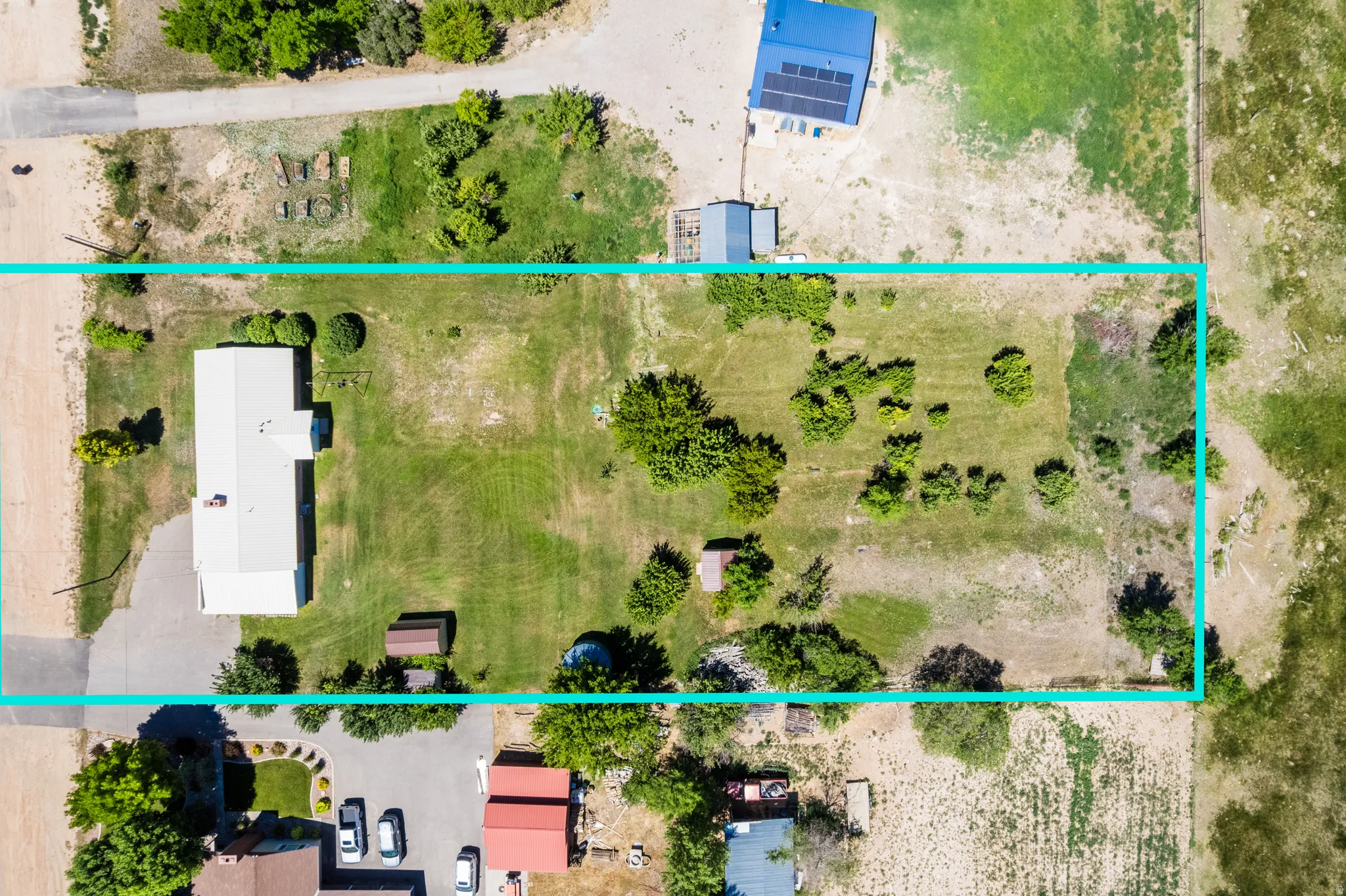 Expansive lot featuring a single-story dwelling with a white roof, gravel driveway, and a mixture of manicured lawn and natural landscaping
