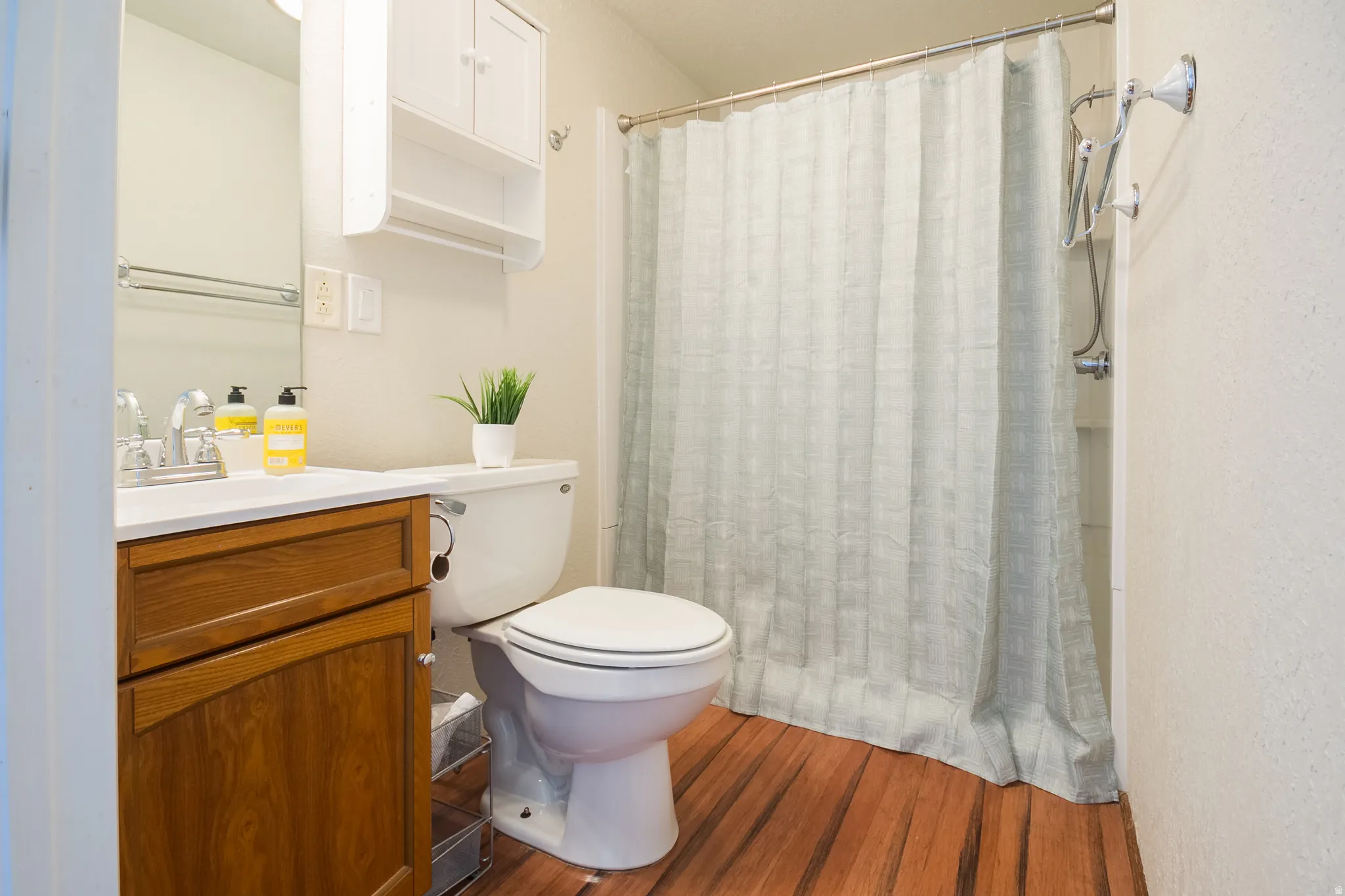 Bathroom featuring wood-finish flooring, a white vanity with an integrated sink, a wall-mounted medicine cabinet, and a shower with a chrome fixture