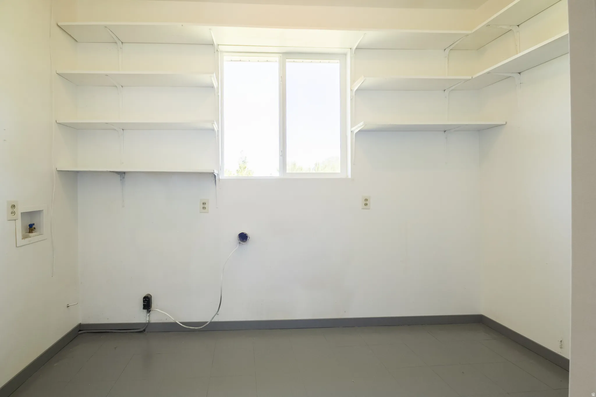 Utility room featuring extensive built-in shelving, a dual-pane window, and grey flooring