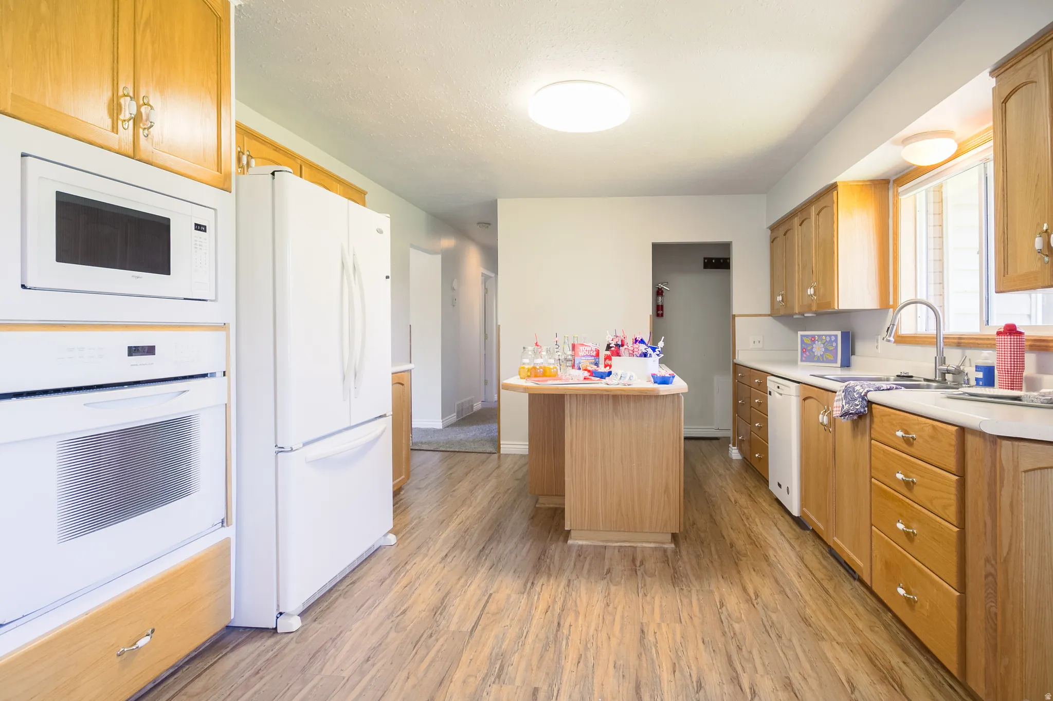 Kitchen featuring wood-finish flooring, light wood cabinetry, white countertops, and a built-in microwave and oven