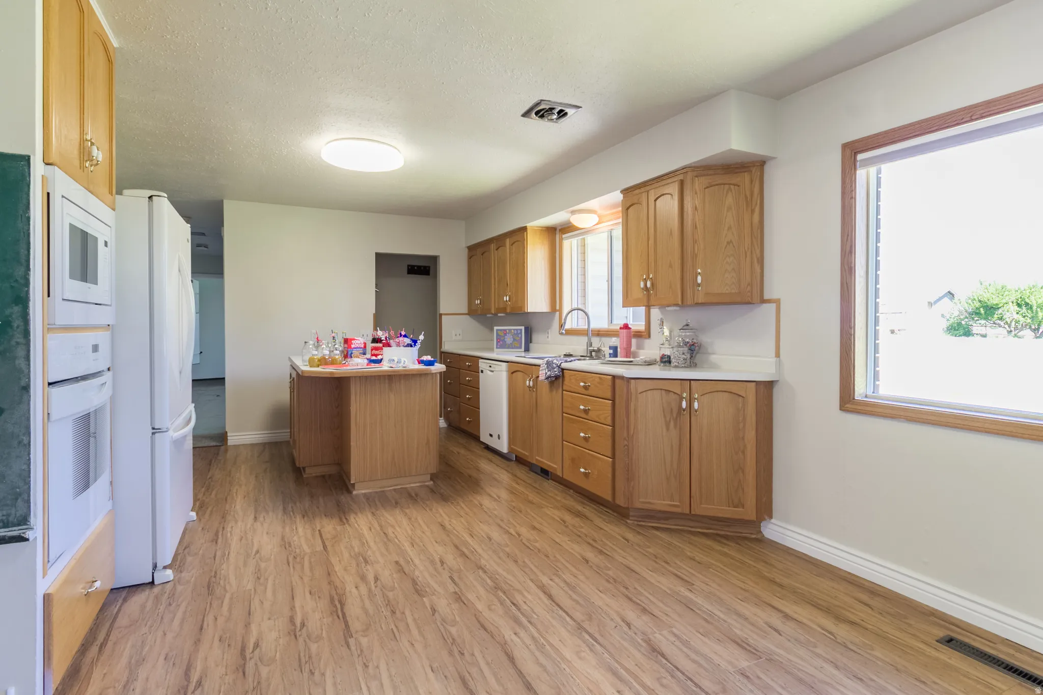 Kitchen featuring wood-finish flooring, light wood cabinetry, white countertops, a built-in oven and microwave, and a central island