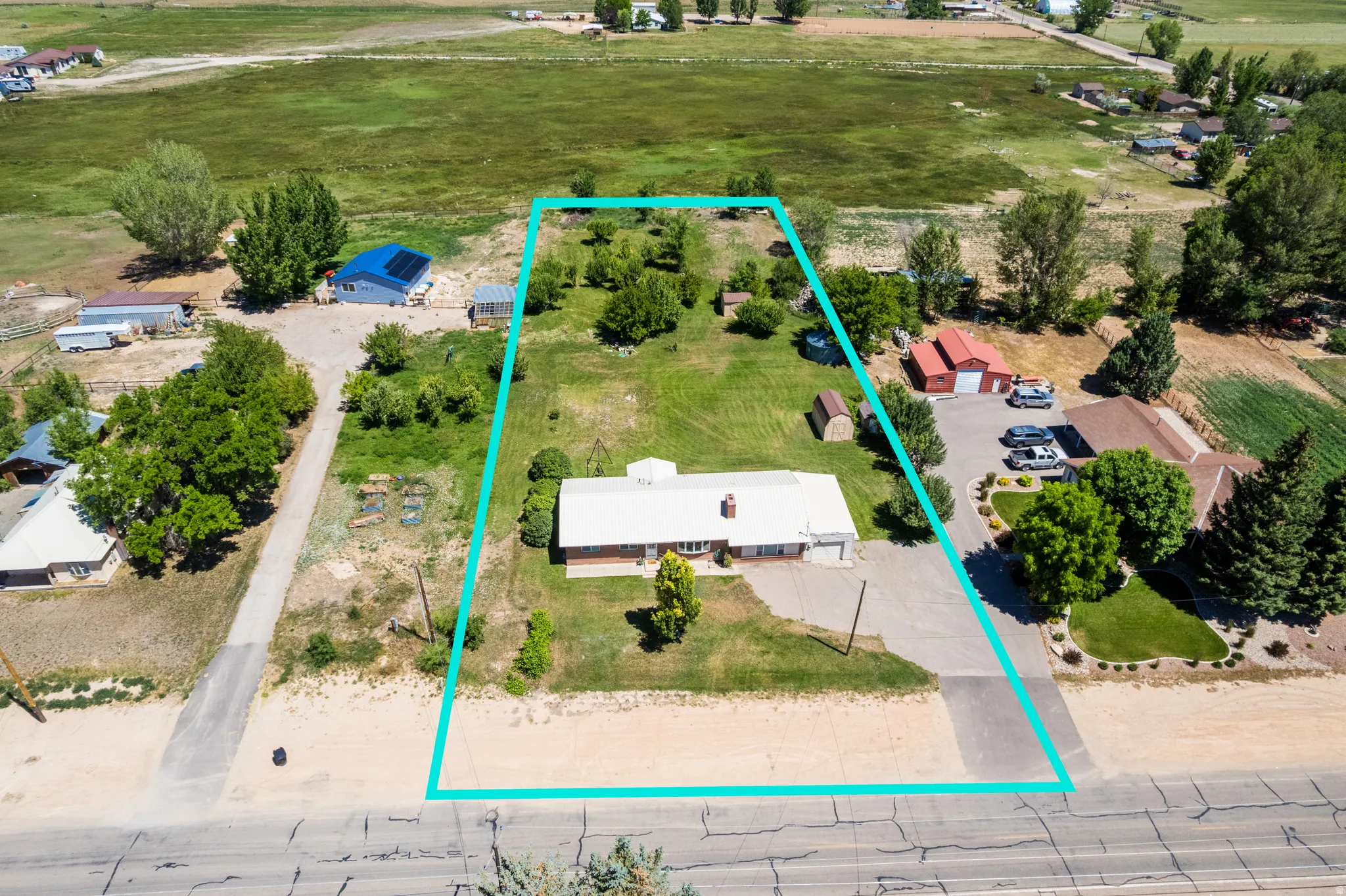 Expansive property featuring a single-story residence with a light-colored roof, a gravel driveway, and mature landscaping