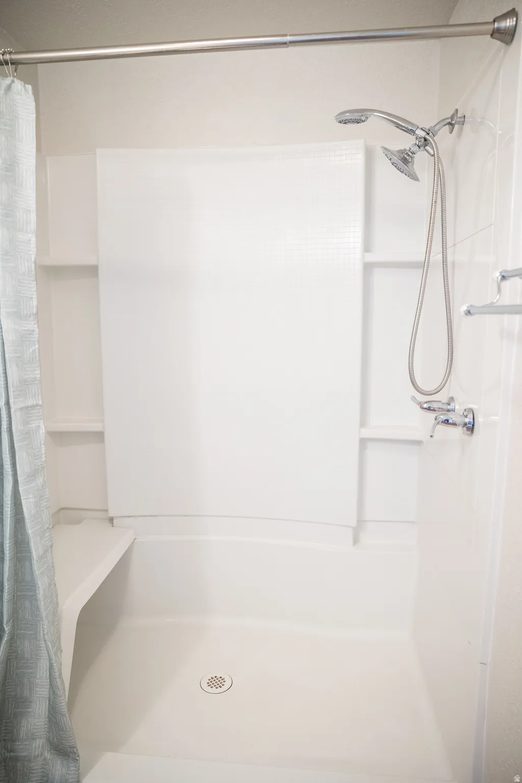 All-white fiberglass shower stall featuring a built-in bench, recessed shelving, a dual shower head system, and a silver shower rod