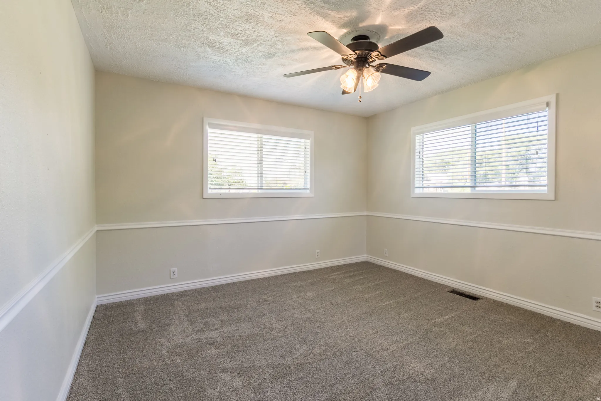 Carpeted room featuring two windows with horizontal blinds, a ceiling fan with integrated lighting, and chair rail molding