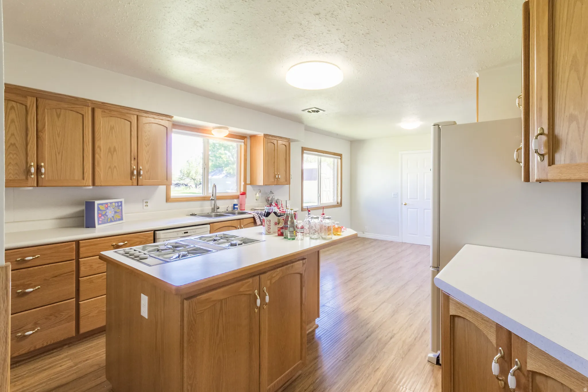 Kitchen featuring light wood cabinetry, white countertops, built-in gas cooktop on an island, wood-finish flooring, and natural light from multiple windows