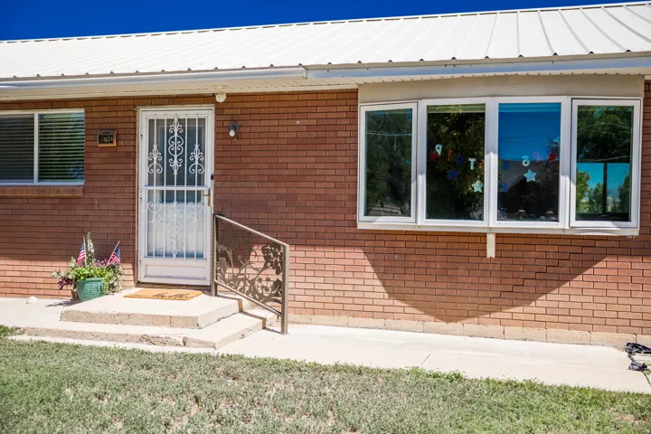 Brick exterior featuring a white metal roof, multiple windows, a security screen door, and a decorative handrail