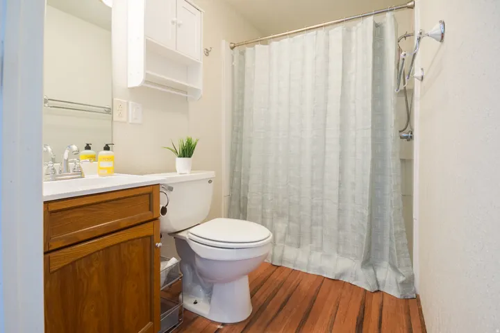 Bathroom featuring wood-finish flooring, a white vanity with an integrated sink, a wall-mounted medicine cabinet, and a shower with a chrome fixture