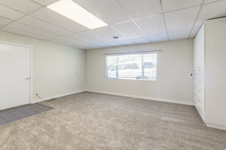 Spacious room featuring neutral carpeting, a large window with horizontal blinds, and extensive built-in cabinetry with multiple drawers and upper storage