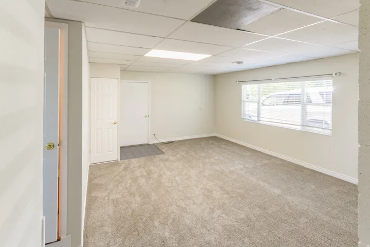 Carpeted room featuring a large window with blinds, drop ceiling, and multiple doors