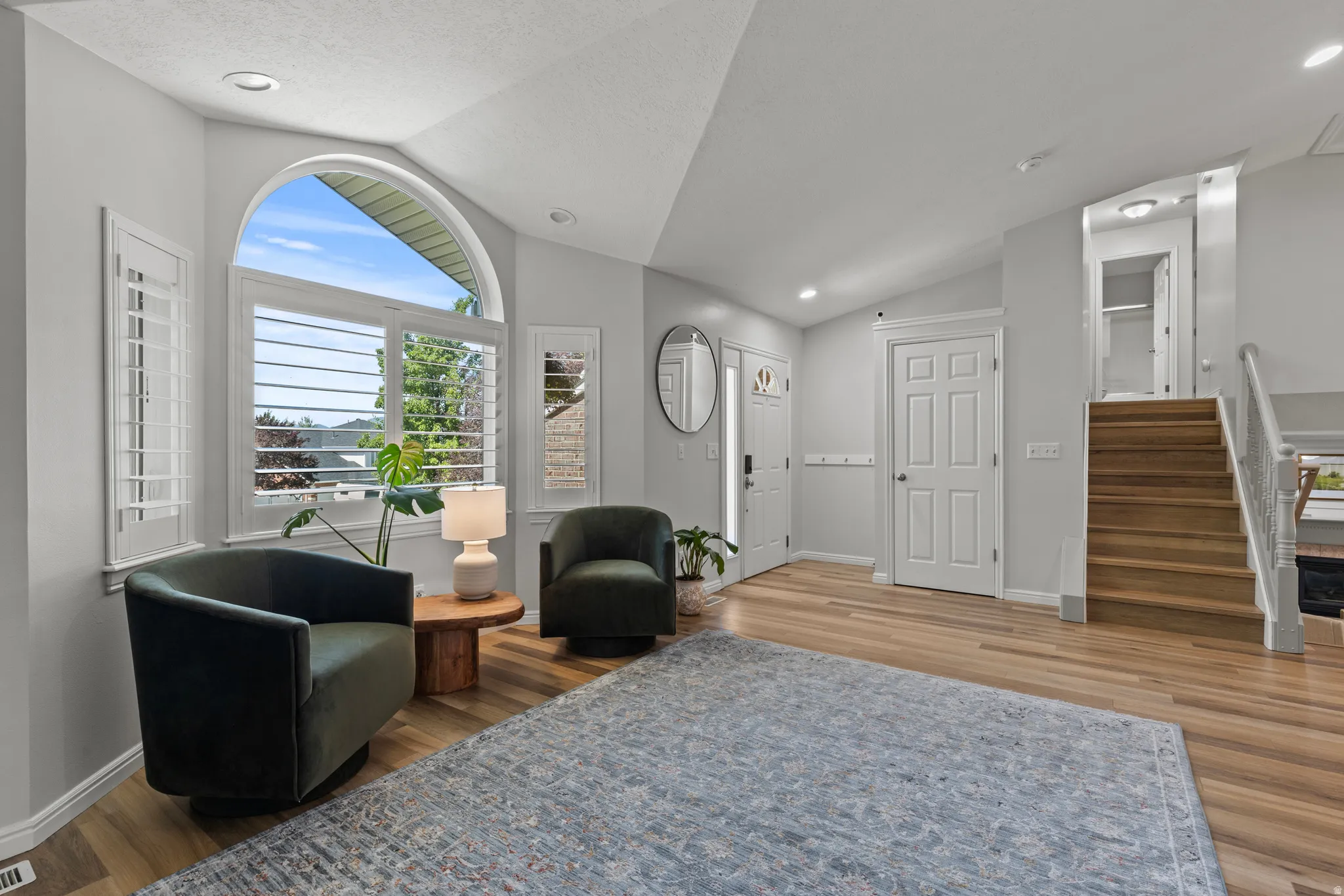 Vaulted ceiling entry with wood-finish flooring, plantation shutters, arched window, and recessed lighting