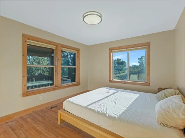 Bedroom featuring wood-finish flooring, two window units with natural wood trim, and a contemporary flush-mount ceiling light