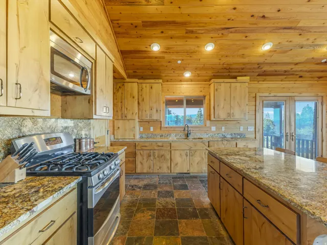 Kitchen featuring wood paneling, wood cabinetry, stone countertops, stainless steel appliances, and multi-toned floor tiles