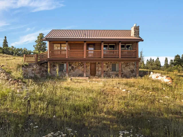 Two-story log home featuring a stone foundation and a second-story wood-railed deck
