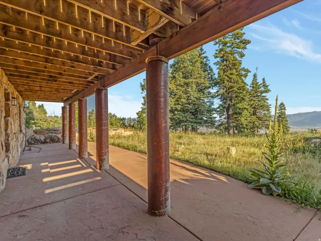 Covered outdoor patio featuring a stamped concrete surface, exposed wood beam ceiling, and stone-clad exterior wall