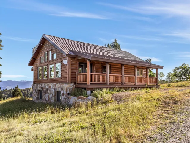 Log cabin exterior featuring a stone foundation, metal roof, wrap-around porch, and multiple windows