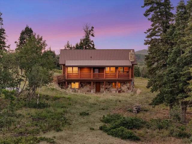 Log cabin exterior featuring a stone foundation, wood siding, and an upper-level balcony