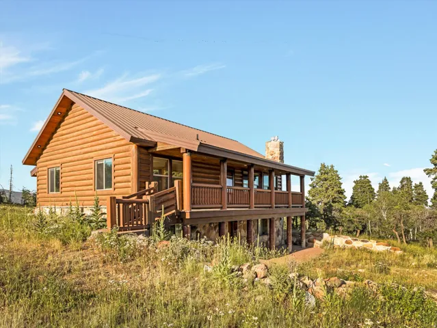 Log cabin exterior featuring a covered porch, stone chimney, and metal roof