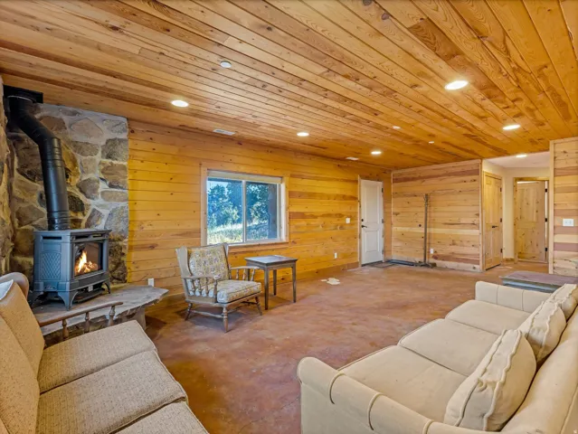 Spacious room featuring wood-finish walls and ceiling, a stone-clad fireplace with a wood-burning stove, and recessed lighting