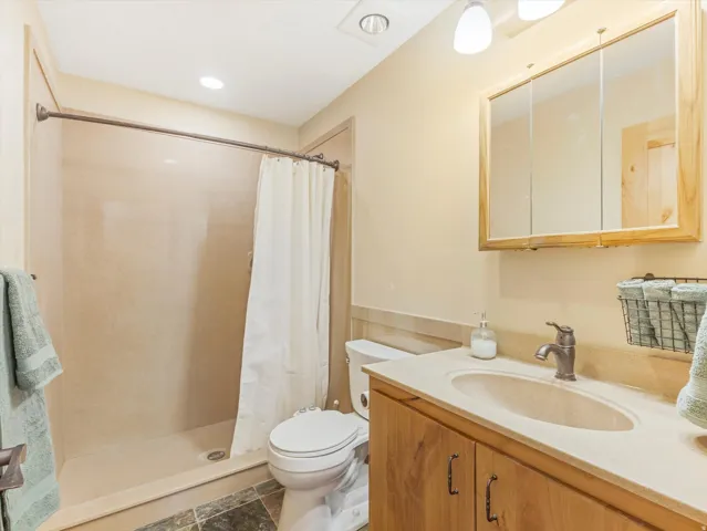 Spacious bathroom featuring a built-in shower with a curved rod, a wood-finish vanity with an integrated sink, a three-panel mirrored medicine cabinet, and dark natural stone tile flooring