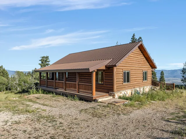 Log cabin exterior with a brown metal roof, full-length covered porch, and a gravel driveway
