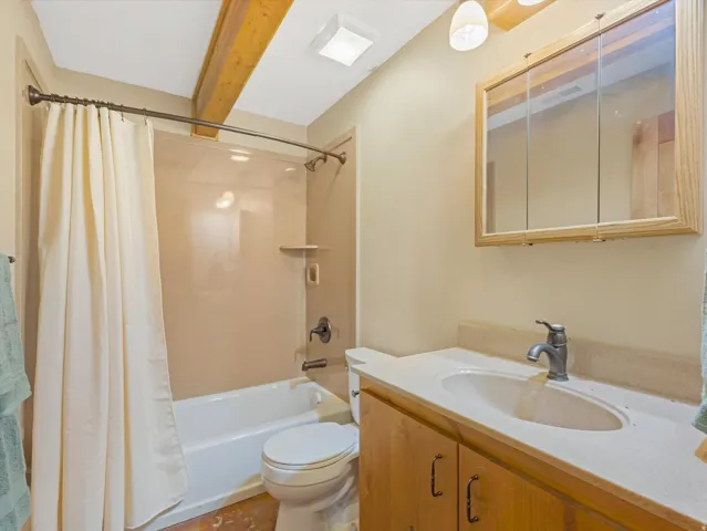Bathroom featuring a vanity with an integrated sink and light-toned countertop, a wood-framed medicine cabinet, and a shower-over-tub combination with a curved shower rod