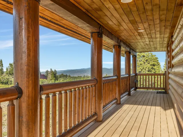 Expansive covered porch featuring a natural wood ceiling, wood-plank flooring, and solid wood log posts