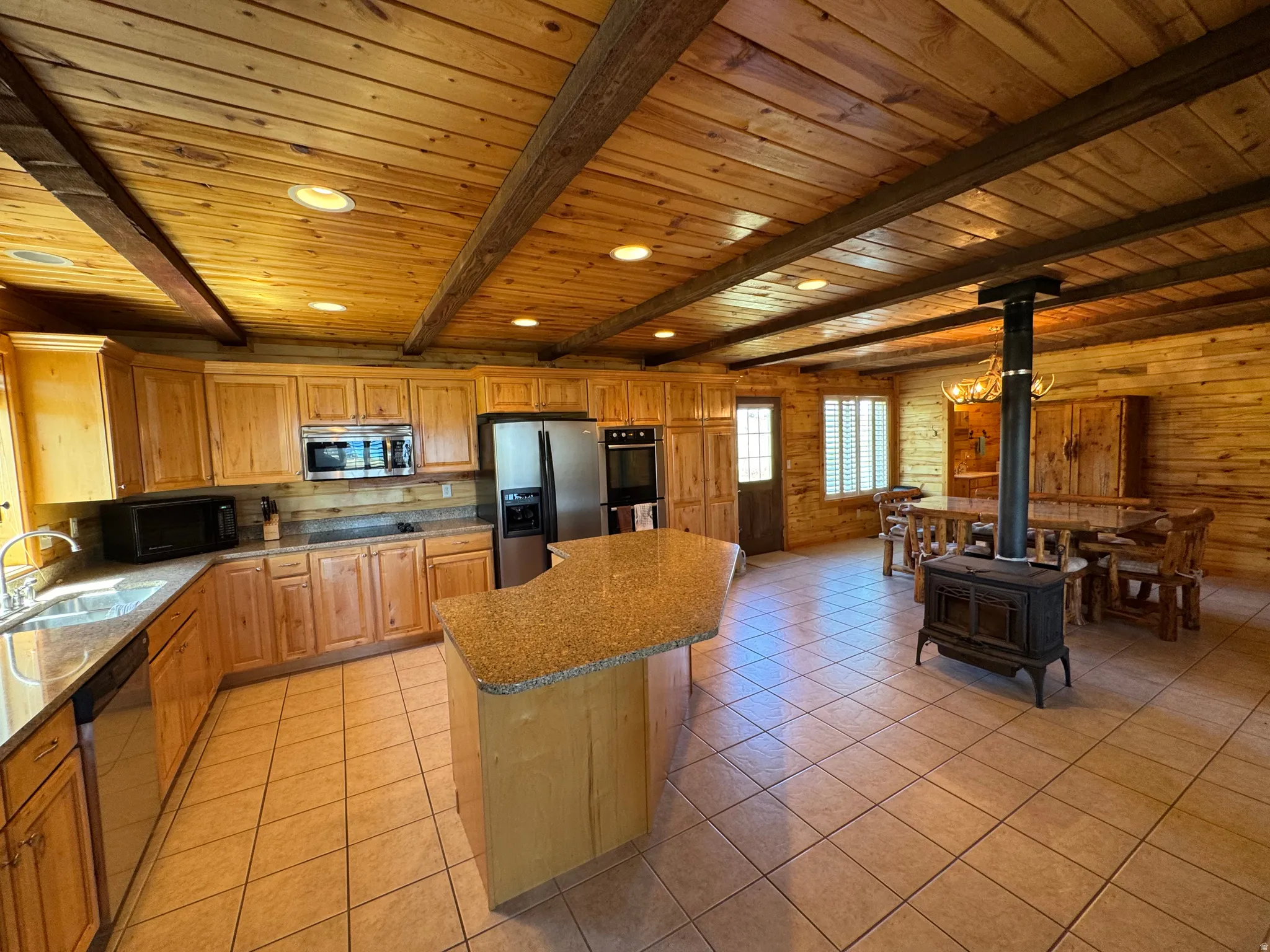 Open-concept kitchen and dining area featuring wood-finish walls and ceiling, exposed wood beams, and recessed lighting