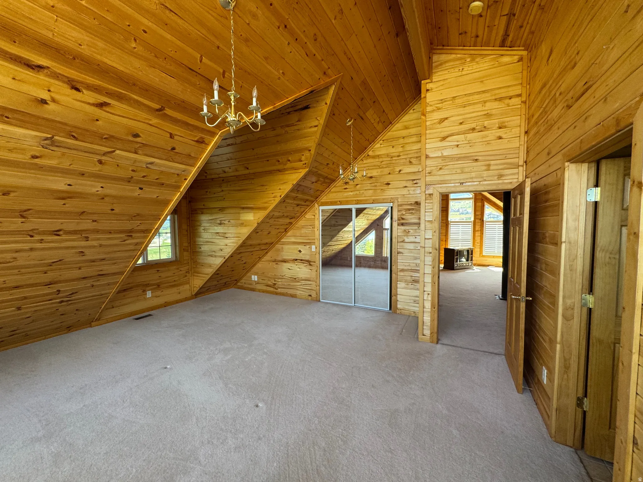 Wood-paneled room featuring a vaulted ceiling and light-colored carpet flooring
