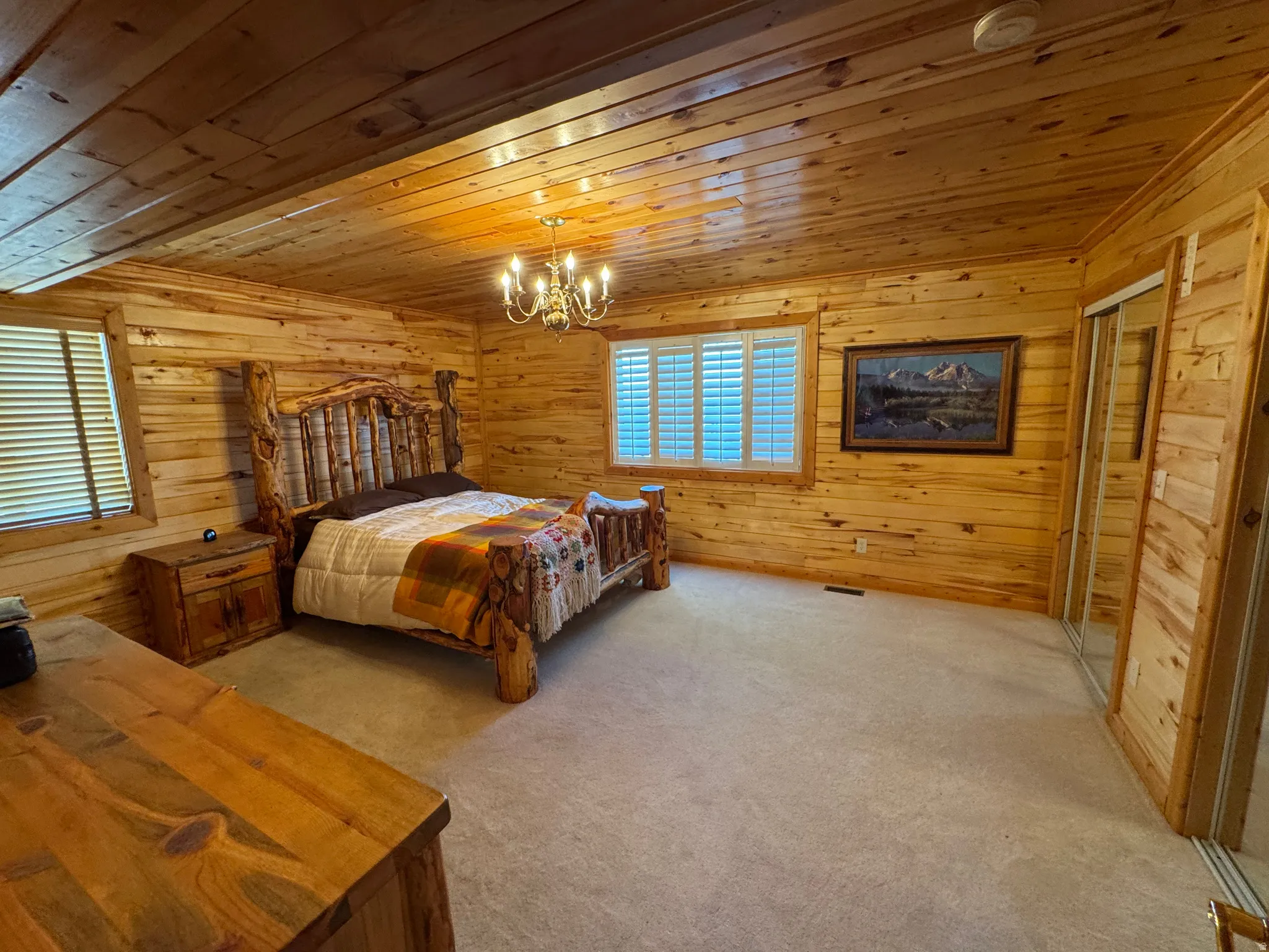 Spacious room featuring wood paneling on walls and ceiling, wall-to-wall carpeting, and a central chandelier