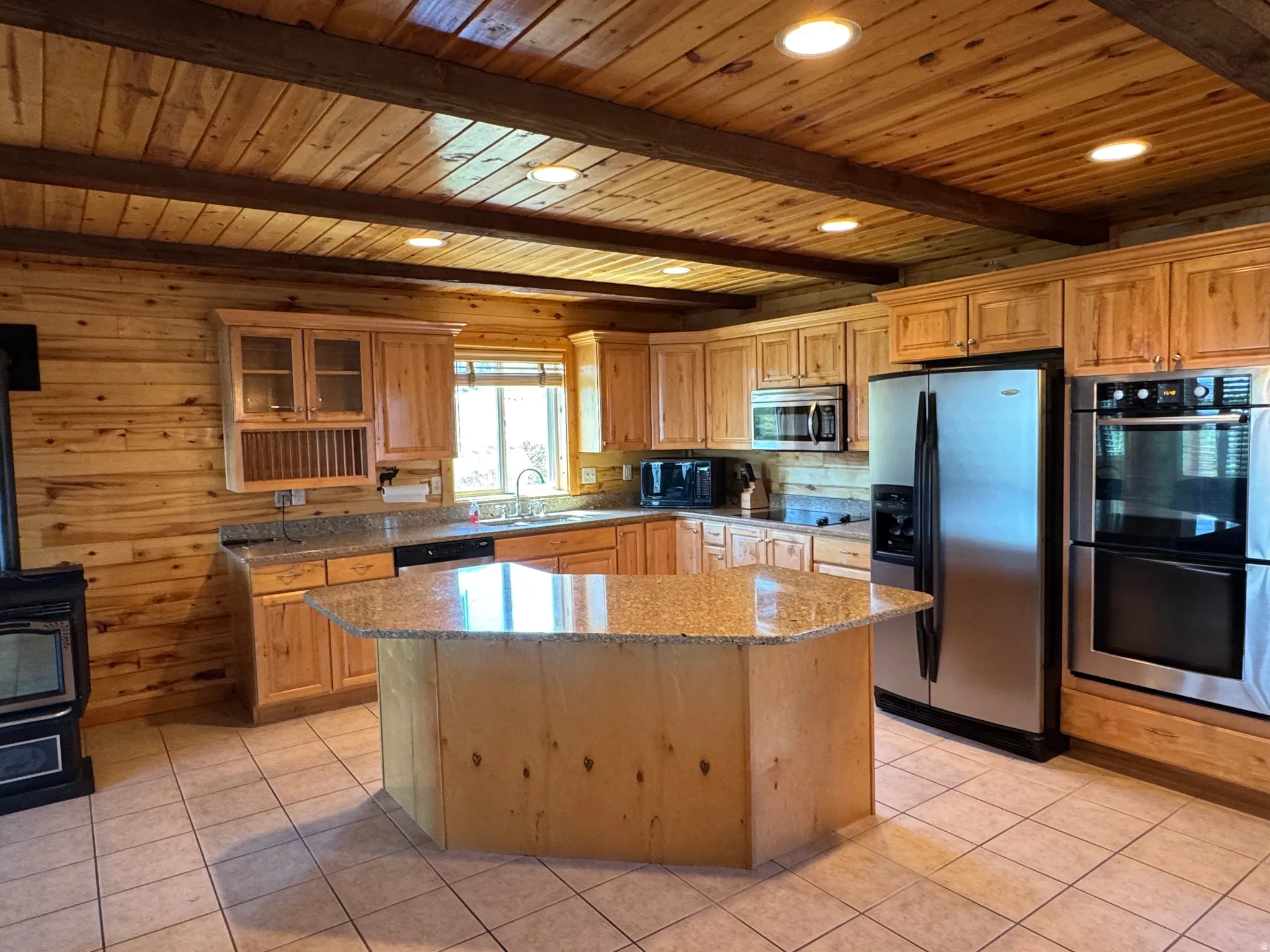 Kitchen featuring wood-paneled walls, wood-finish ceiling with exposed beams, recessed lighting, tile flooring, and a central island with a granite-style countertop