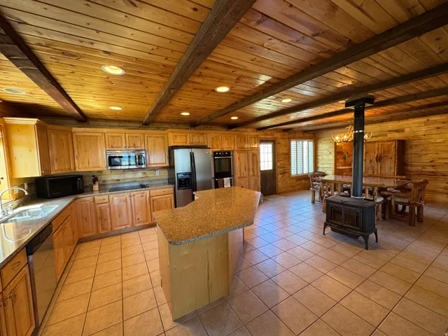 Open-concept kitchen and dining area featuring wood-finish walls and ceiling, exposed wood beams, and recessed lighting